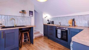A modern kitchen with a wooden countertop, a sink, and a staircase leading to an upper level. - The Vault - Boutique Cosy Peak District Retreat in a Grade II listed building (Chapel-en-le-Frith)