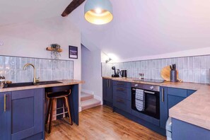 A modern kitchen with a wooden countertop, a sink, and a staircase leading to an upper level. - The Vault - Boutique Cosy Peak District Retreat in a Grade II listed building (Chapel-en-le-Frith)