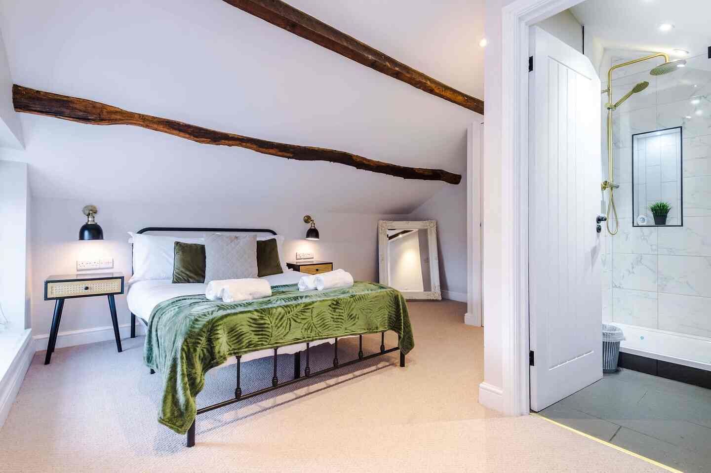 A bedroom with a bed, bedside tables, a mirror, a nightstand, and a bathroom with a shower.