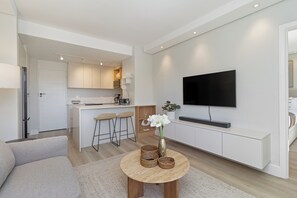 A modern living room with a sofa, a coffee table, and a TV mounted on the wall. - Light and Modern | Designer Sea Point Gem (Cape Town)