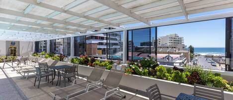 A rooftop terrace with outdoor seating, a pool, and a view of the ocean and buildings.
