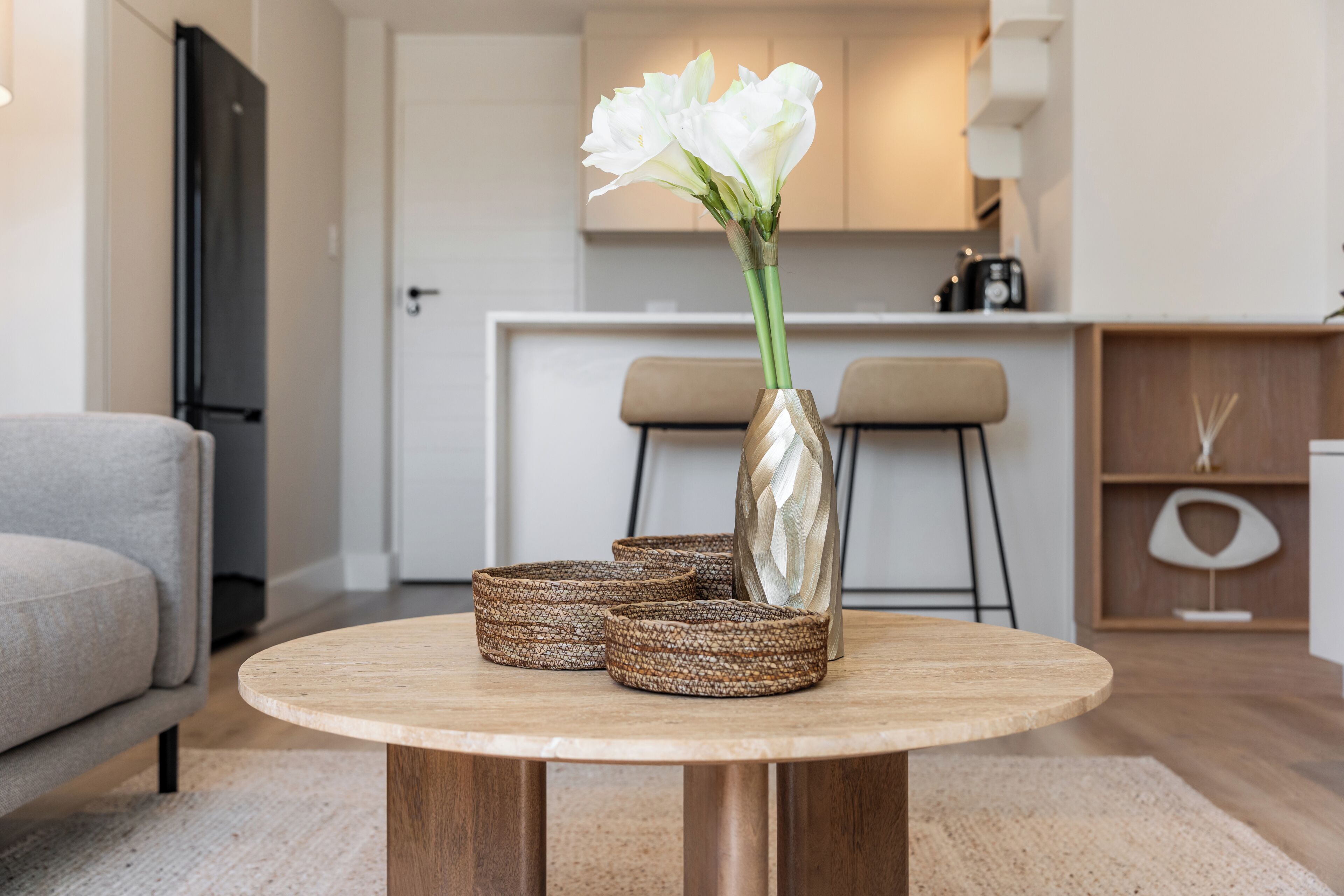 Une table ronde en bois, ornée d’un vase de fleurs blanches et de deux paniers en osier.