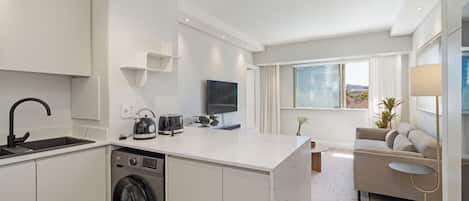 A modern kitchen with a built-in washing machine, a flat-screen TV, and a dining area with a sofa and a small table.