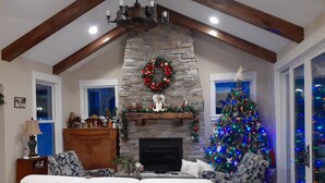 A living room with a stone fireplace, a Christmas tree, and a white sofa. - 4 BR beach house with Swim Spa, Steam Shower & 42 ft playroom. Sleeps 9 (Maple Lake)