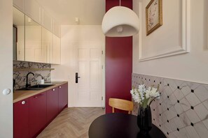 A compact kitchen with a marble backsplash, a wooden dining table with a vase of flowers, and a pendant light. - Bema Atelier Bath & Marble Suite | Near Beach (Sopot)