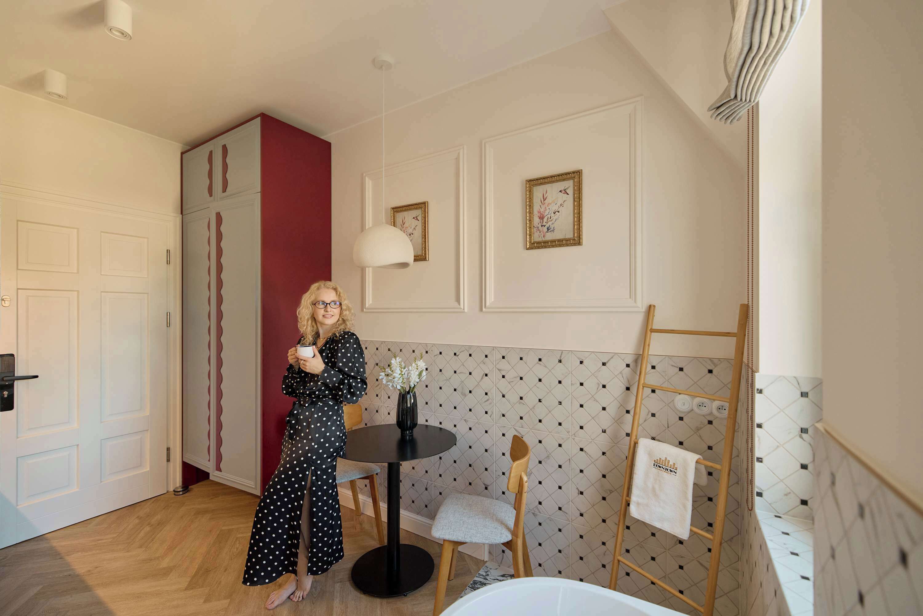 A room with a wooden floor, a round table with a chair, a white door, and a red accent wall.