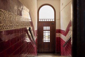 A staircase with a wooden door and a window, leading to a room with red-tiled walls and a decorative metal railing. - Bema Atelier Bath & Marble Suite | Near Beach (Sopot)