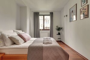Ein Hotelzimmer mit einem Bett, einem Nachttisch mit Lampe, einer Topfpflanze und gerahmten Bildern an der Wand.