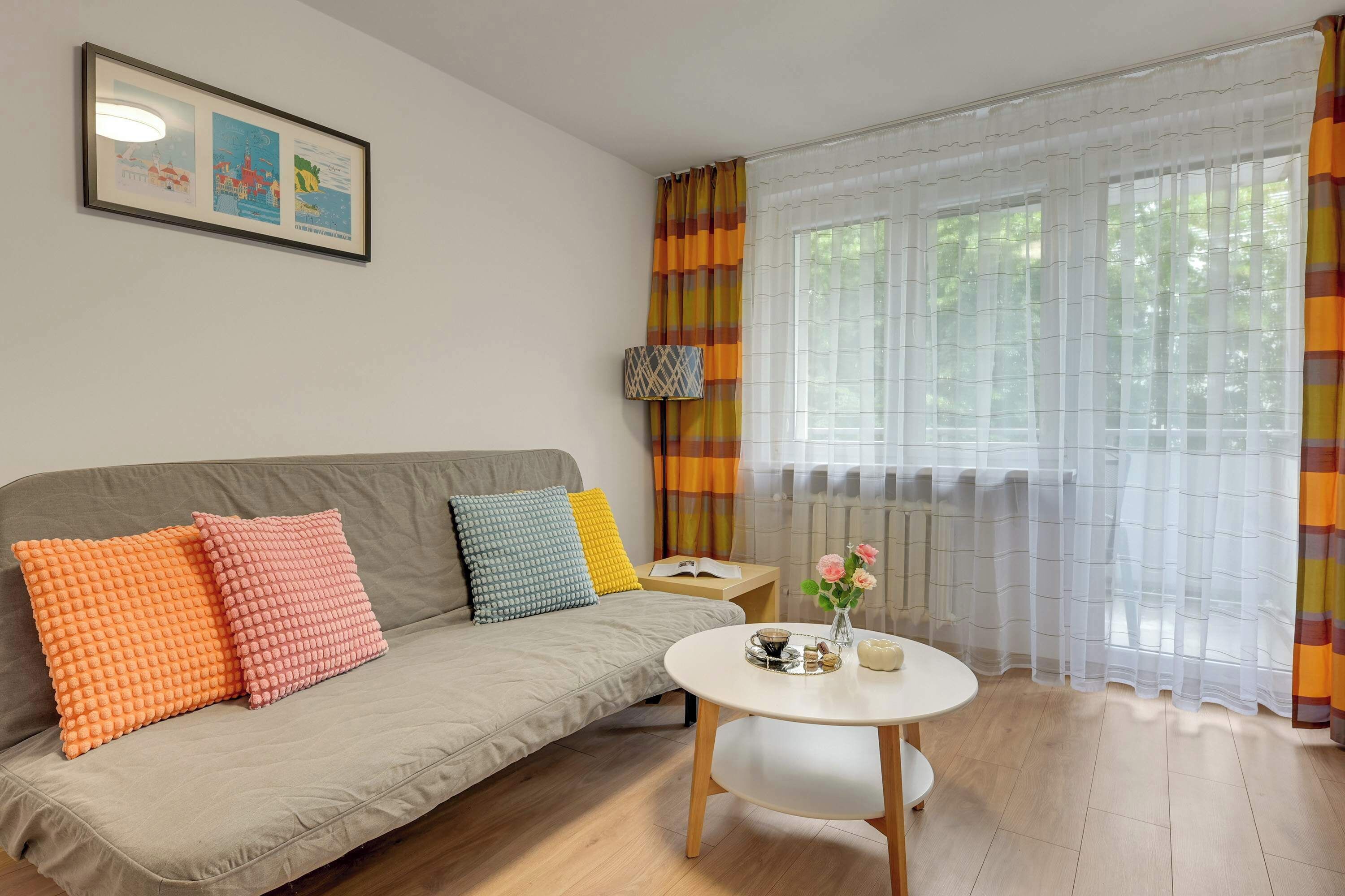 A living room with a sofa, pillows, a coffee table, a lamp, and a window with curtains.