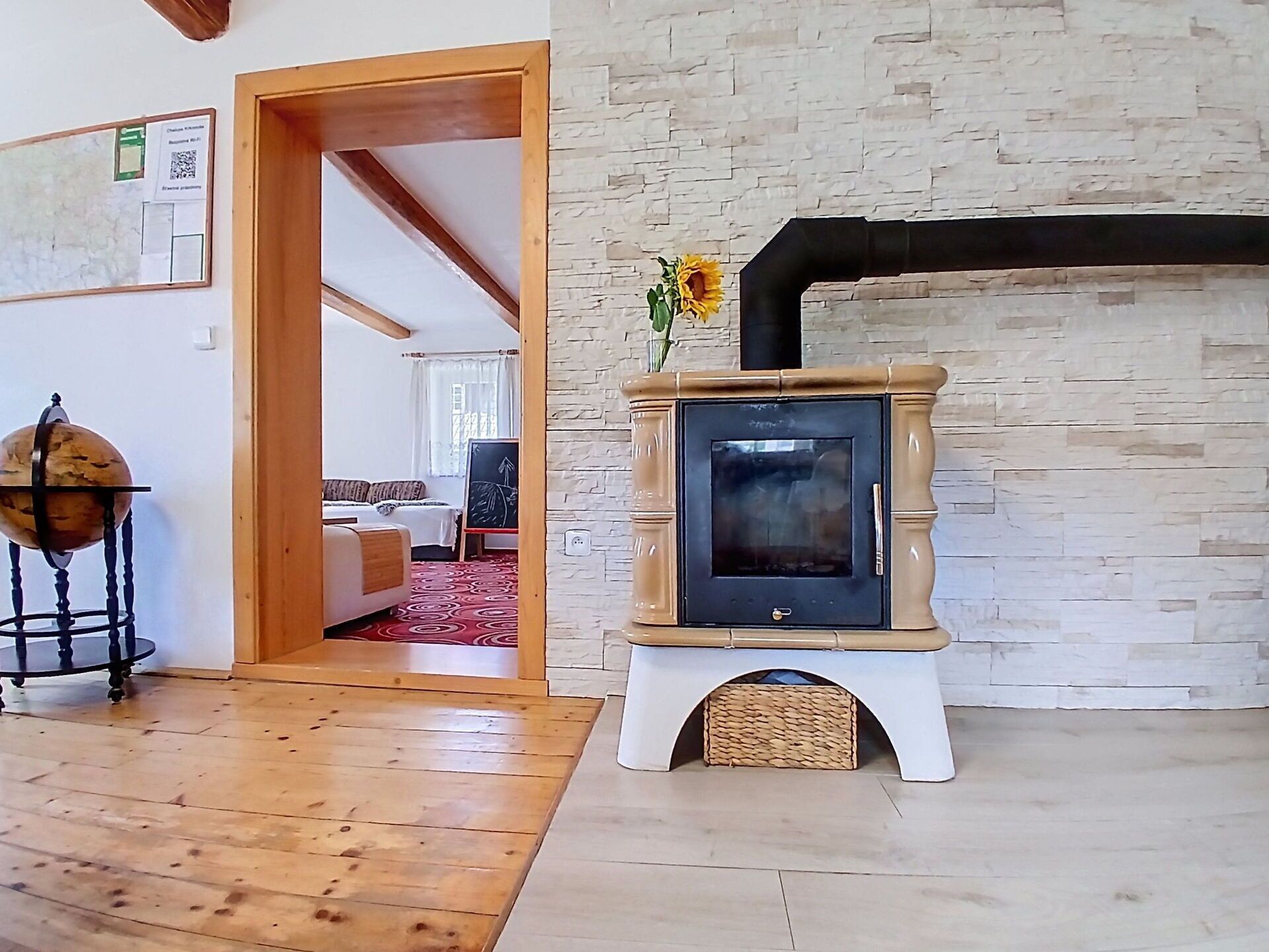 A room with a wooden floor, a stone wall, a fireplace, and a door leading to another room.