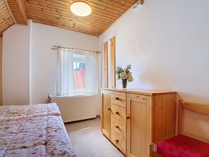 A bedroom with a wooden bed, a dresser, a mirror, and a window with curtains.