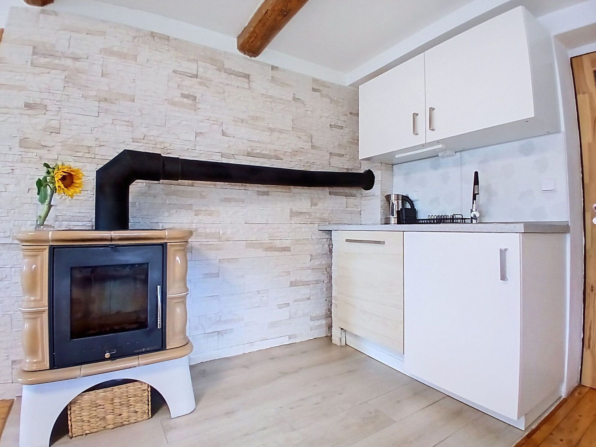 A kitchen with a wood-burning stove, white cabinets, and a stone wall.