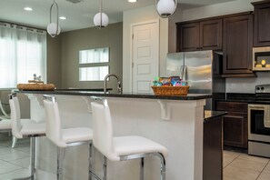 A kitchen with a central island, bar stools, stainless steel appliances, and a window with blinds. - Luxury Disney Escape - Pool, SPA and Games (Kissimmee)