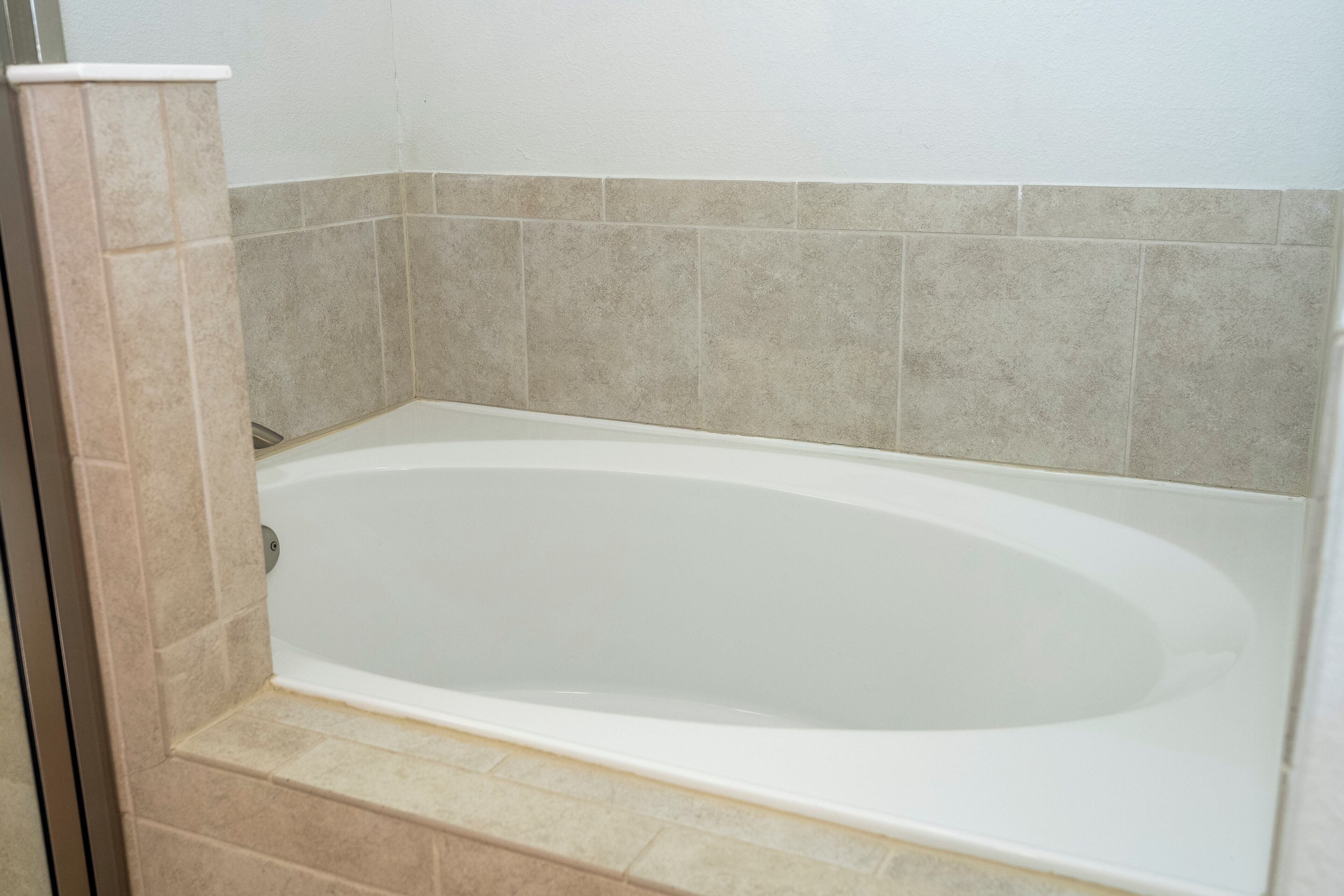 A bathtub with a white interior, beige tiles on the walls, and a beige base.