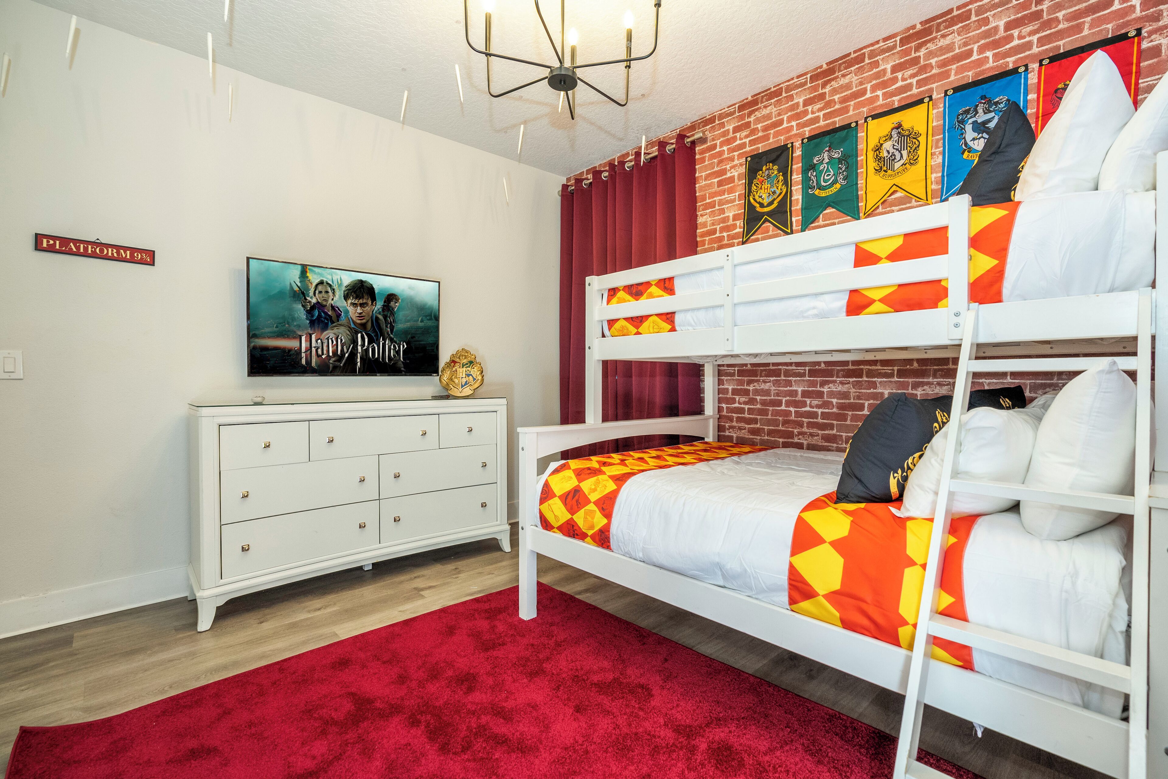 Een kamer met een stapelbed, een flatscreen televisie, een witte ladekast en een rood tapijt.