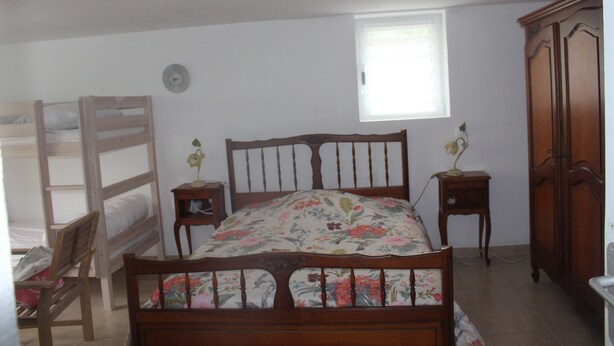 A bedroom with a wooden bed, a window, a wardrobe, a bedside table, and a chair. - Holiday Home 'Maison Vue Sur La Tour' with Private Terrace, Wi-Fi and Air Conditioning (Montcuq-en-Quercy-Blanc)