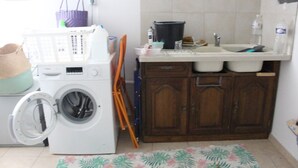 A compact kitchen with a washing machine, a sink, and wooden cabinets. - Holiday Home 'Maison Vue Sur La Tour' with Private Terrace, Wi-Fi and Air Conditioning (Montcuq-en-Quercy-Blanc)
