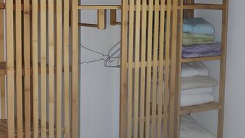 Une armoire en bois, dotée de plusieurs étagères et d’une tringle à vêtements, contenant des vêtements pliés et une petite boîte de rangement.