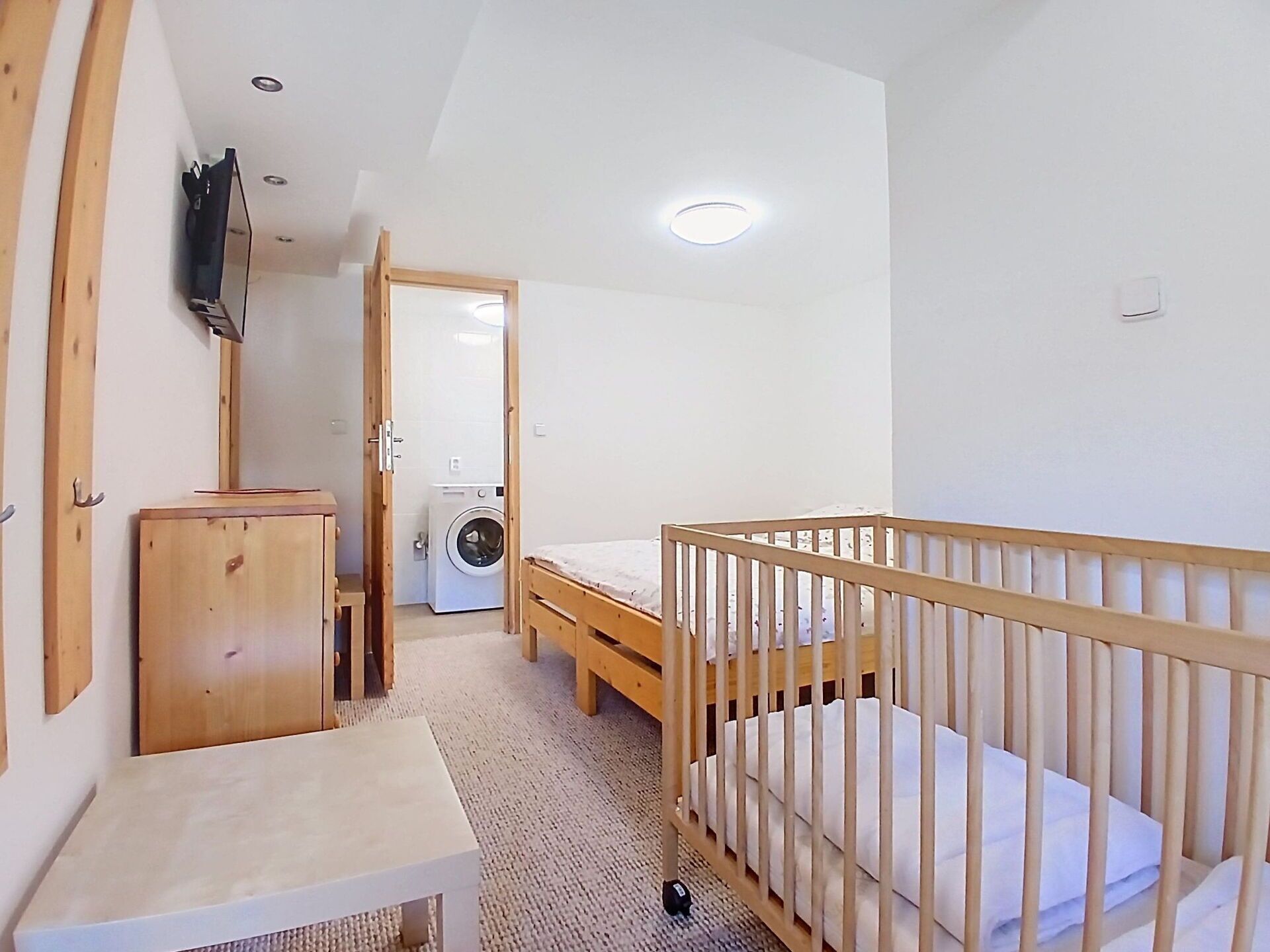 A room with a crib, a washing machine, and a small table.