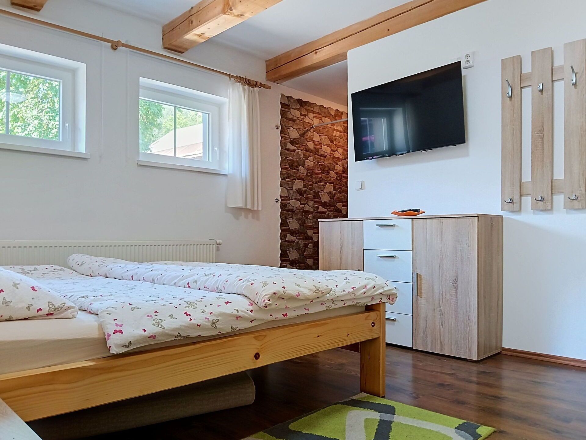 A bedroom with a bed, a TV mounted on the wall, a wardrobe, and a stone wall.