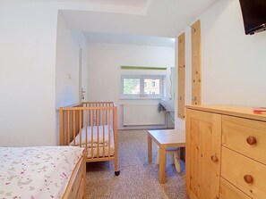 A room with a crib, a desk, and a wardrobe.