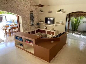 A modern living room with a stone wall, a flat-screen TV, and a dining area with a table and chairs. - 4BR Tropical Villa with Private Pool - 2 Min to Beach (Las Terrenas)