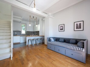 Um interior moderno com piso de madeira, uma cozinha compacta, um espaço de jantar e uma área de estar com um sofá xadrez.