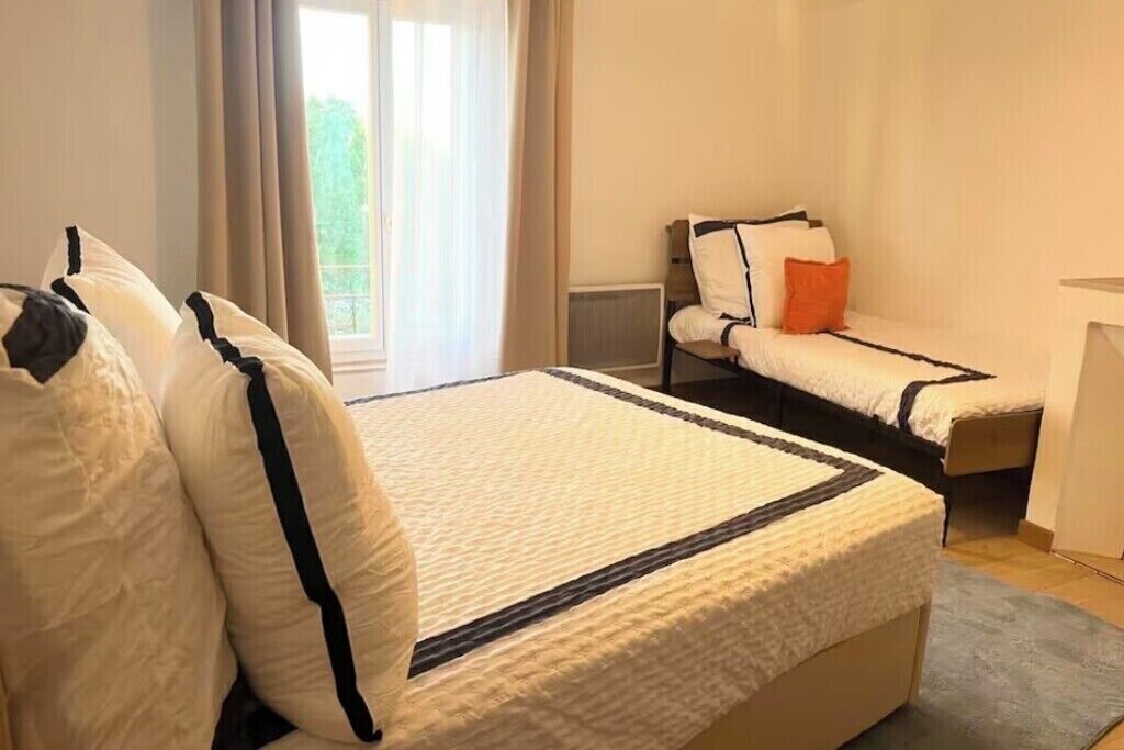 Un dormitorio con una cama grande, dos camas más pequeñas, una mesita de noche y un ventanal con cortinas.