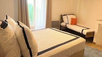 Un dormitorio con una cama grande, dos camas más pequeñas, una mesita de noche y un ventanal con cortinas.