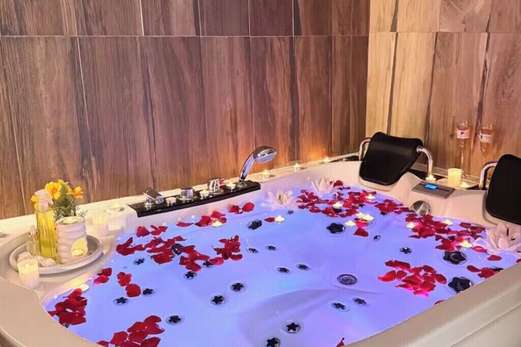 Bany d'hidromassatge amb pètals de rosa, espelmes i un arranjament floral.