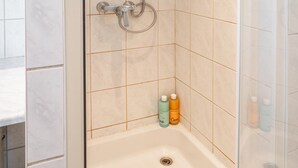 Una ducha a nivel con puerta de cristal, cabezal de ducha de mano y rociador de mano.