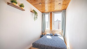 Un dormitorio con techo de madera, una cama con colcha estampada, dos mesitas de noche y una ventana con cortinas.