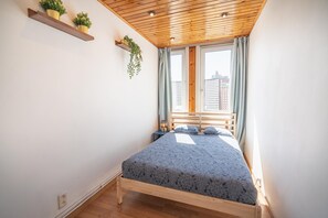Um quarto com teto de madeira, uma cama com colcha estampada, duas mesas de cabeceira e uma janela com cortinas.