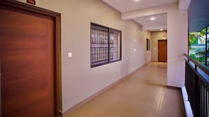 A hallway with a wooden door marked '102', a window with metal bars, and a balcony with a railing. - Cocostay Kozhikode (Kozhikode)