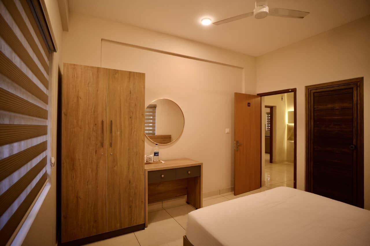 A bedroom with a bed, a wooden wardrobe, a desk with a mirror, and a ceiling fan.