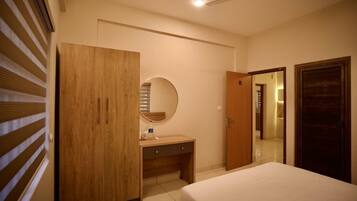 A bedroom with a bed, a wooden wardrobe, a desk with a mirror, and a ceiling fan.