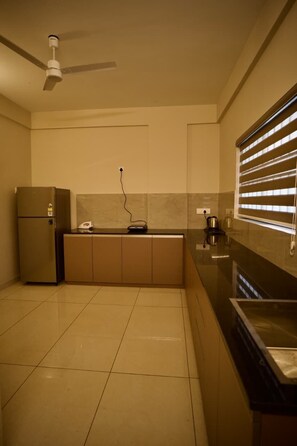A compact kitchen with a built-in refrigerator, a countertop with a kettle, and a ceiling fan. - Cocostay Kozhikode (Kozhikode)