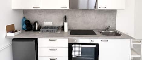 Cocina moderna con armarios blancos, horno integrado, lavavajillas y encimera con varios electrodomésticos.