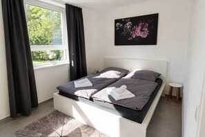 Un dormitorio moderno con cama, mesita de noche y ventana con cortinas.