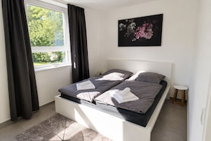 Un dormitorio moderno con cama, mesita de noche y ventana con cortinas.