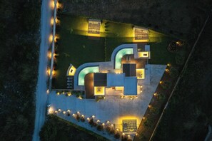 Uma casa moderna com uma entrada em curva, piscina e fachada bem iluminada.