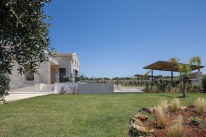 Ein modernes Haus mit einer Stein-Fassade, einer Terrasse mit Gartenmöbeln und einem gepflegten Rasen.