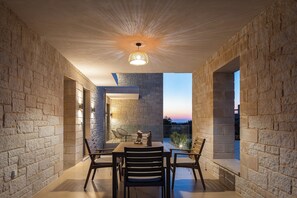 Uma área de refeições com parede de pedra, mesa, cadeiras e luminária pendente.