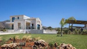 Uma casa moderna com fachada de pedra, área de estar coberta ao ar livre e gramado bem cuidado.