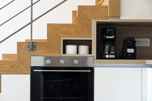 Cozinha com forno embutido, cafeteira e prateleira de madeira com duas rolos de papel toalha.