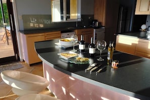 A modern kitchen with a curved island, a dining area with chairs, and a view of the outdoors.