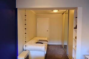 A small, narrow room with a bed, a bedside table, and a mirror.