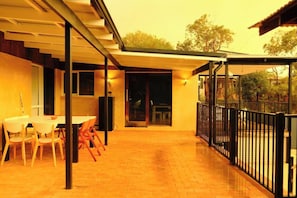 A covered outdoor area with a table and chairs, a glass door leading to a room, and a fenced garden area.