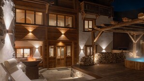A wooden cabin with a fireplace, lounge chairs, and a hot tub.