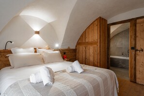 Une chambre à coucher avec un grand lit, une armoire en bois et une salle de bain visible à travers une porte ouverte.